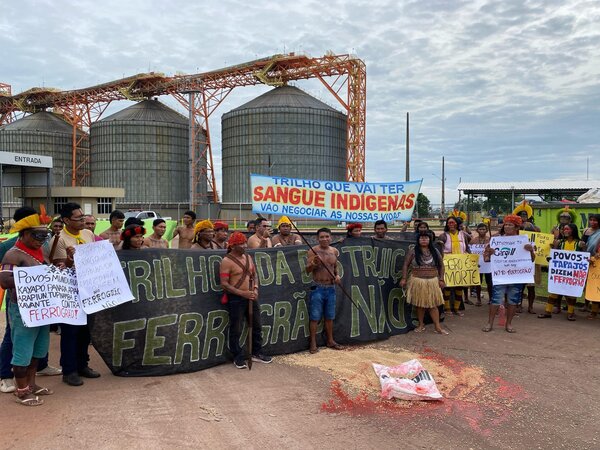 fotografia de um grupo de indígenas durante a ocupação da Cargill, portando cartazes e com um saco de soja aberto no chão