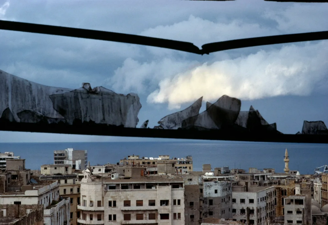 foto da cidade de Beirute, no Líbano, tirada de dentro de um prédio com uma janela destruída, com o mar mediterrâneo ao fundo