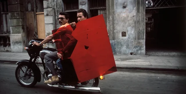 fotografia de dois homens em uma motocicleta, um deles segurando um vidro vermelho